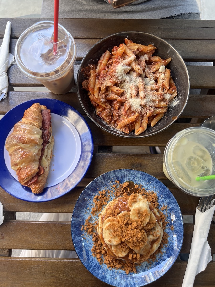 A table at Neama with pasta, a bacon croissant, pancakes and iced drinks