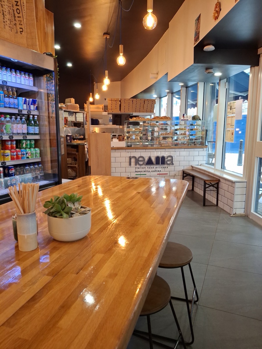 Inside Neama: the tiled counter with the neama logo, pastry cases and the long oak table